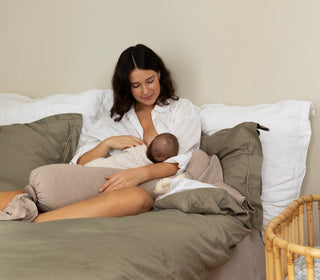 Woman breastfeeding a baby on a bed with a neutral color palette