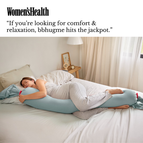 Woman lying on a bed with a blue body pillow, surrounded by neutral decor.