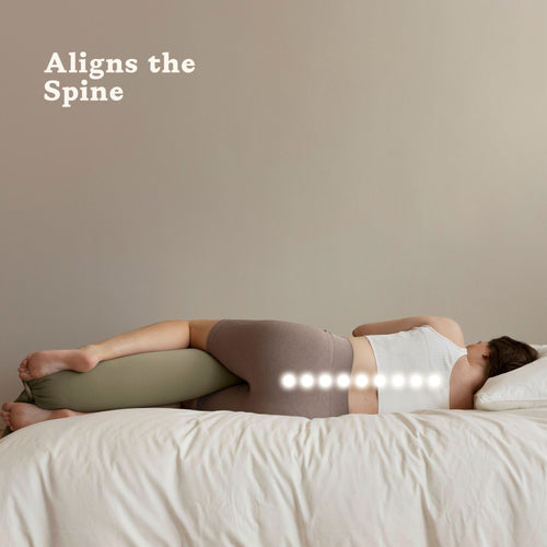 Woman lying down in bed with a pregnancy pillow between her knees with text that says "Aligns the spine"