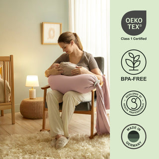 Woman holding a baby with a pink cushion in a room, featuring Oeko-Tex and BPA-Free certification bbhugme pregnancy pillow.