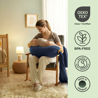 Woman holding a baby in a room with Oeko-Tex, BPA-Free, and Made in Germany certification bbhugme pregnancy pillow on the right.