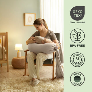 Woman holding a large pillow in a cozy room with Oeko-Tex and BPA-Free certification logos bbhugme pregnancy pillow on the right.